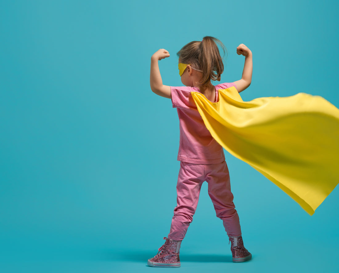 Une petite fille avec une cap jaune de super-héroïne sur fond bleu